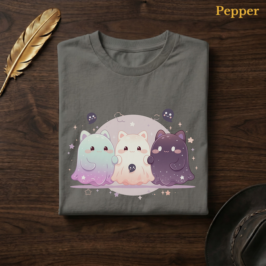 Dreamy ghost shirt in Pepper, a warm grey-charcoal garment-dyed shirt folded flat on dark walnut wood beside a gold feather and a leather hat, the Ghoul Friends galaxy design centred on the chest, labelled Pepper.