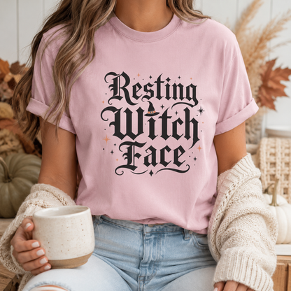 Witchy humor tee in Blossom worn by a woman holding a ceramic coffee mug, styled with pumpkins, dried leaves, and a cozy knit cardigan, the Resting Witch Face design centred on the chest.