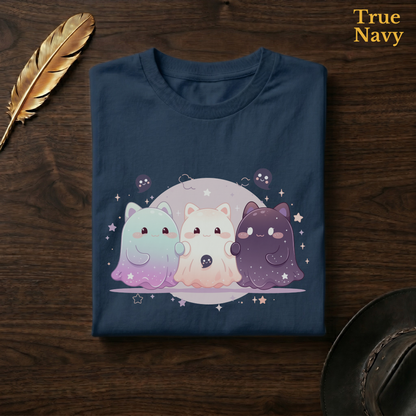 Celestial cat tee in True Navy, a deep navy garment-dyed shirt folded flat on dark walnut wood beside a gold feather and a leather hat, the moonlit cat-ghost trio design on the chest, labelled True Navy.
