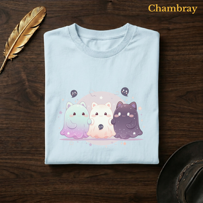 Ghoul Friends tee in Chambray, a soft pale blue garment-dyed shirt folded flat on dark walnut wood beside a gold feather and a leather hat, the starry cat-ghost trio design on the chest, labelled Chambray.
