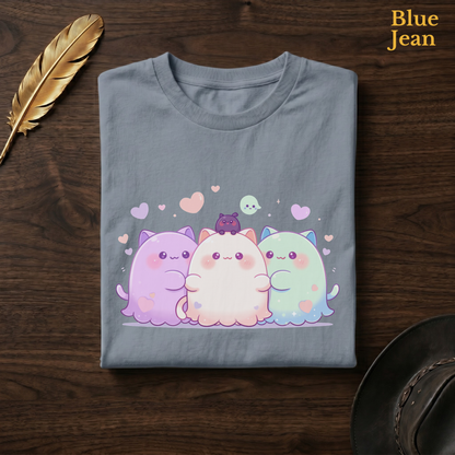 Cat ghost trio gift tee in Blue Jean, a faded denim-blue garment-dyed shirt folded flat on dark walnut wood beside a gold feather and a leather hat, the Ghoul Friends blob design on the chest, labelled Blue Jean.