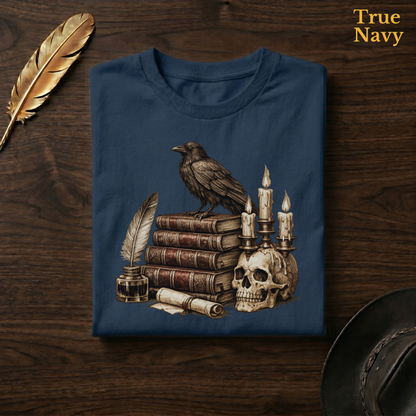 Poe's Study tee in True Navy, a deep navy garment-dyed shirt folded flat on dark walnut wood beside a gold feather and a leather hat, the raven and skull candelabra design on the chest, labelled True Navy.
