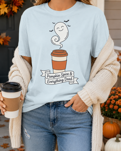 Cozy halloween shirt in light blue worn by a woman in a cream cardigan holding a to-go coffee cup, standing on a porch with fall leaves, mums, and pumpkins, the ghost latte design and Pumpkin Spice & Everything Dead banner on the chest.