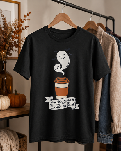 Pumpkin spice shirt in Black on a wooden hanger in a cozy fall interior, with white and orange pumpkins, a dried leaf arrangement, and cardigans on a clothing rack nearby, the ghost latte and banner design centred on the chest.