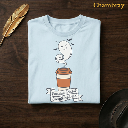 Pumpkin Spice & Everything Dead tee in Chambray, a soft pale blue garment-dyed shirt folded flat on dark walnut wood beside a gold feather and a leather hat, the ghost latte design on the chest, labelled Chambray.