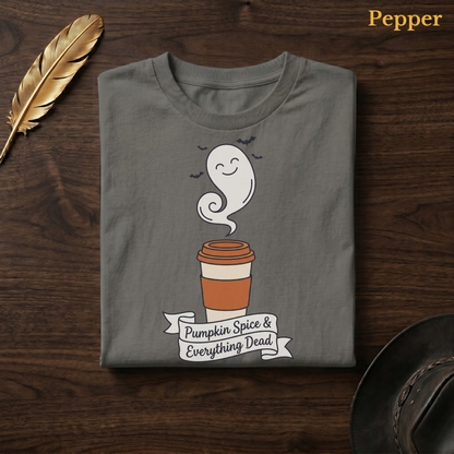 Spooky season shirt in Pepper, a warm grey-charcoal garment-dyed shirt folded flat on dark walnut wood beside a gold feather and a leather hat, the ghost latte design centred on the chest, labelled Pepper.