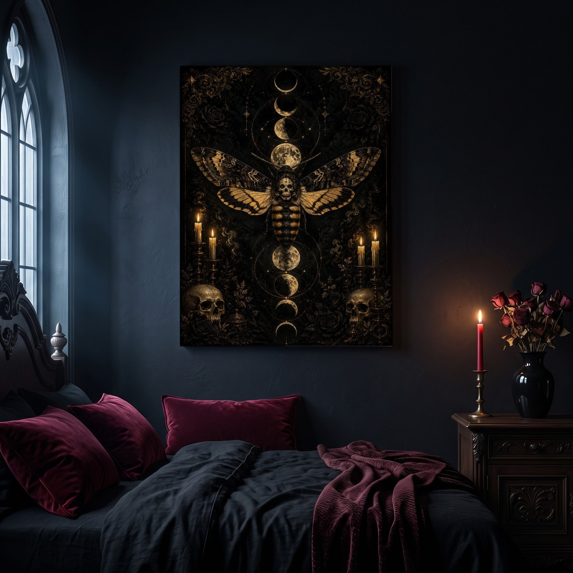 Acherontia moth canvas hanging on a dark navy wall in a gothic bedroom, above a bed with burgundy velvet pillows and charcoal bedding, beside an arched leaded window and a wooden nightstand holding a lit red taper candle in a brass holder and a black vase of dried roses.