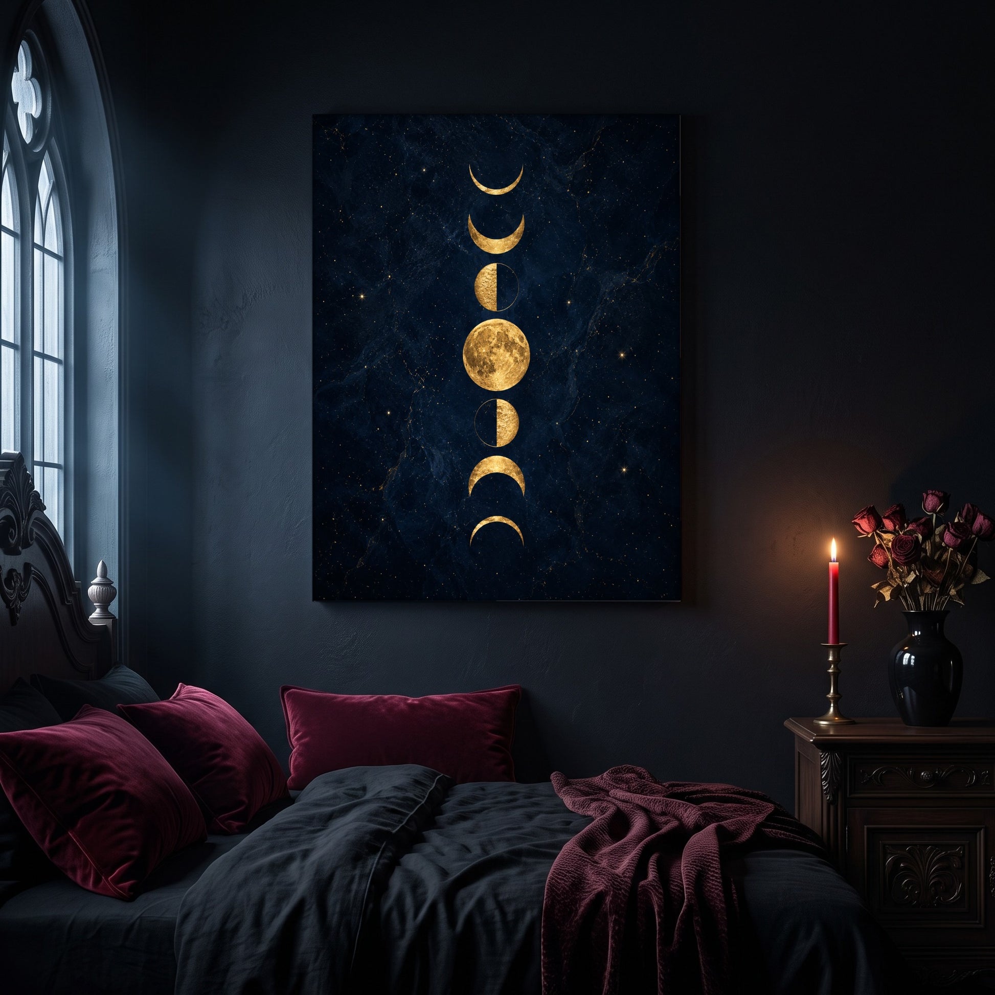 Lunarium gold moon phase canvas hanging on a dark navy wall in a gothic bedroom, above a bed with burgundy velvet pillows and charcoal bedding, beside an arched leaded window and a wooden nightstand holding a lit red taper candle in a brass holder and a black vase of dried roses.