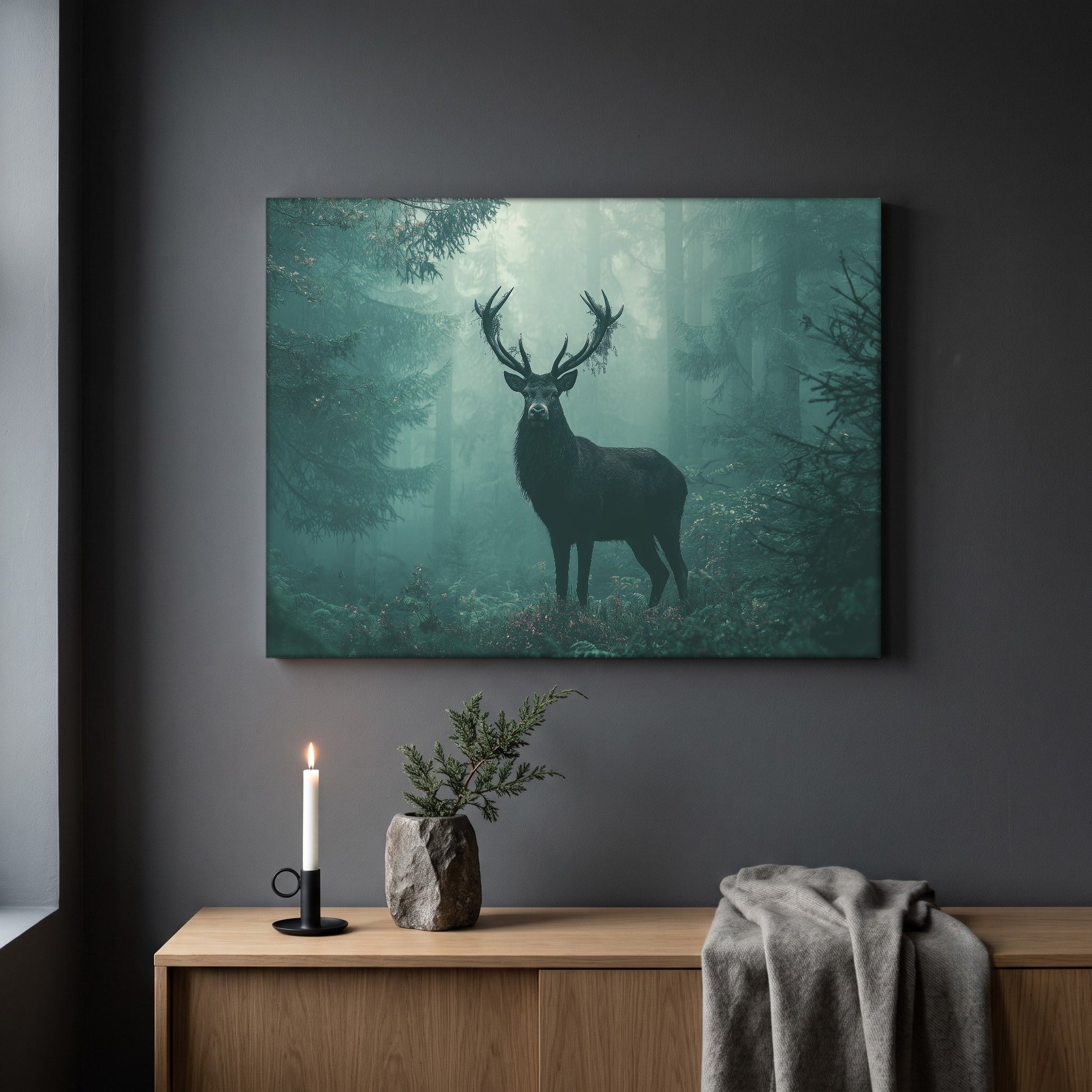 The Green Chapel woodland print hanging on a plain dark grey wall above a light oak sideboard, styled with a lit white taper candle in a black holder, a stone vase of juniper, and a soft grey throw draped over the end.