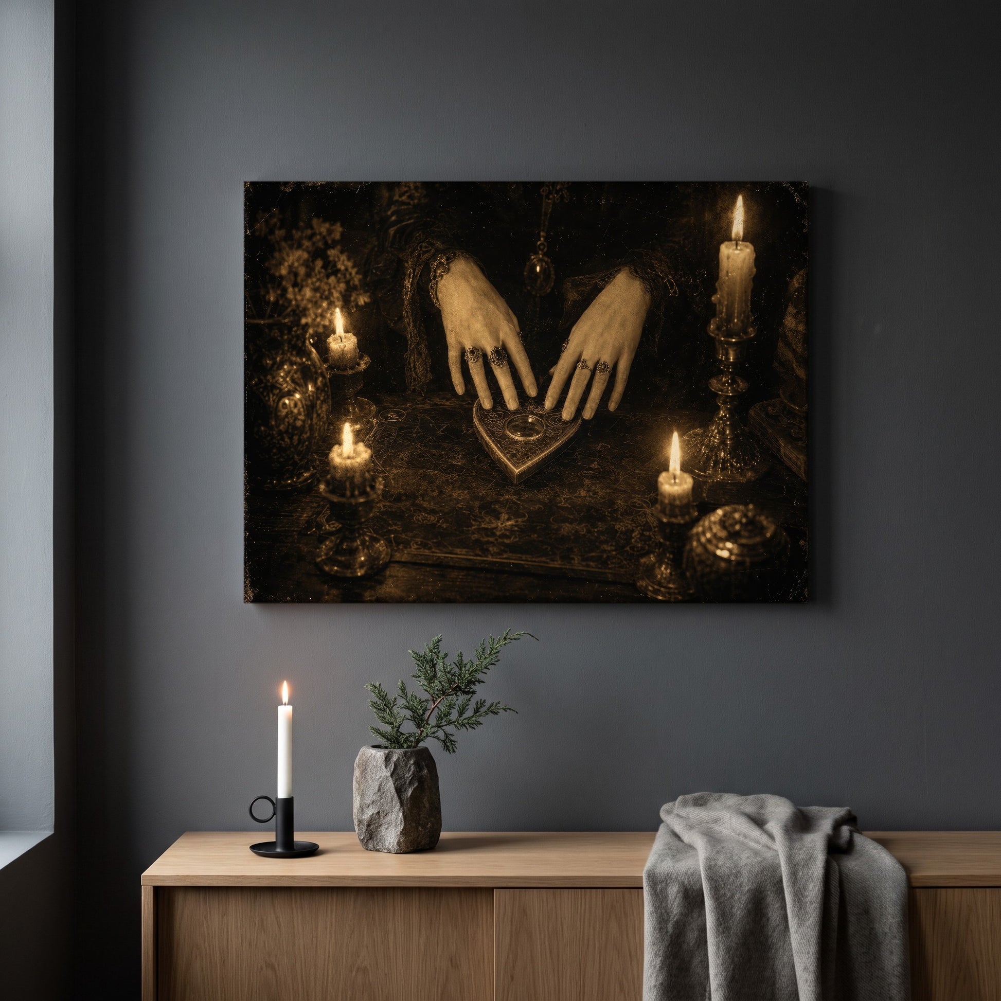 Midnight Communion print hanging on a plain grey wall above a light oak sideboard, styled with a black candlestick holding a lit white taper candle, a small stone vase with a juniper sprig, and a folded grey throw.