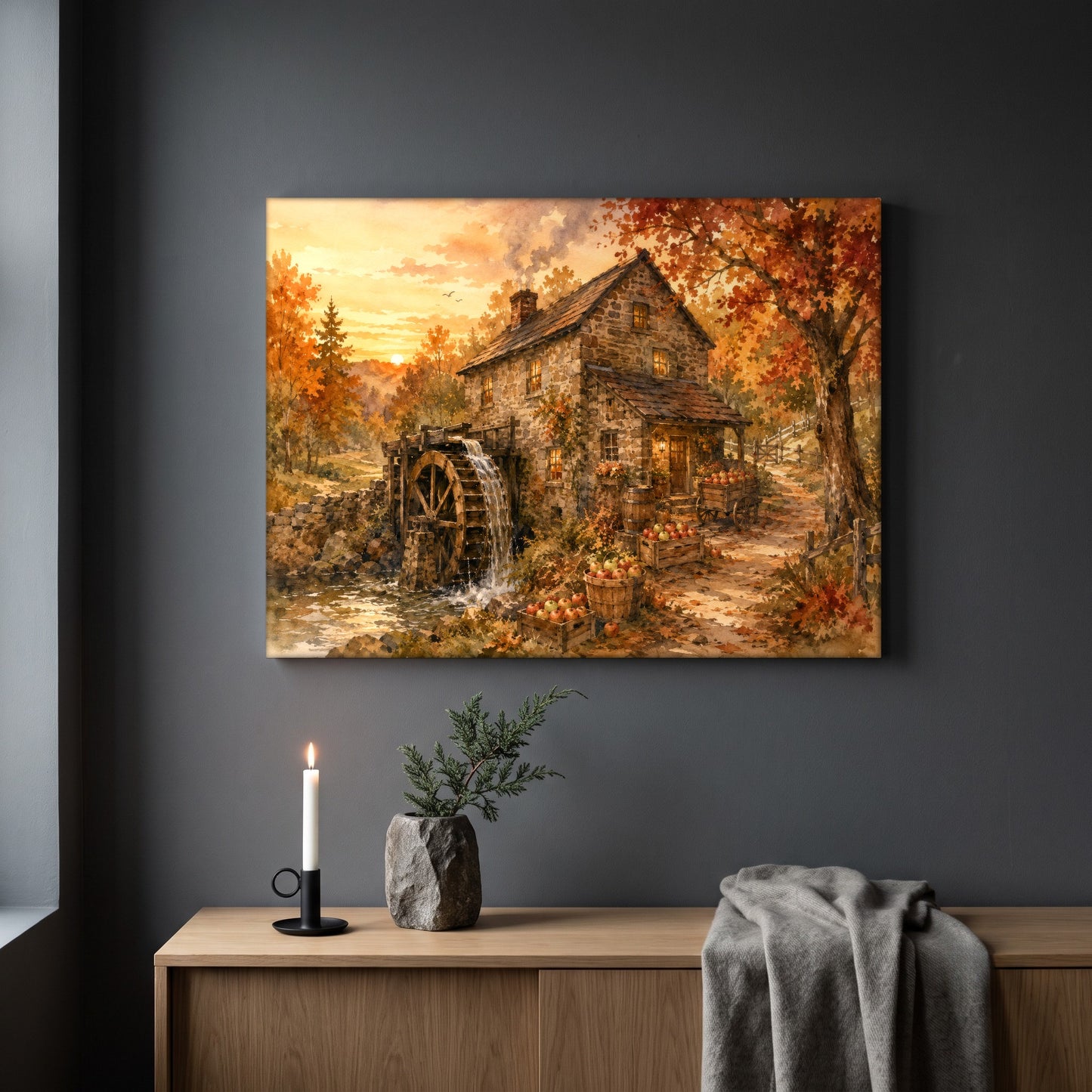 Millpond Gold watermill canvas hanging on a plain grey wall above a light oak sideboard, styled with a lit white taper candle in a black holder, a small stone pot of greenery and a folded grey throw.