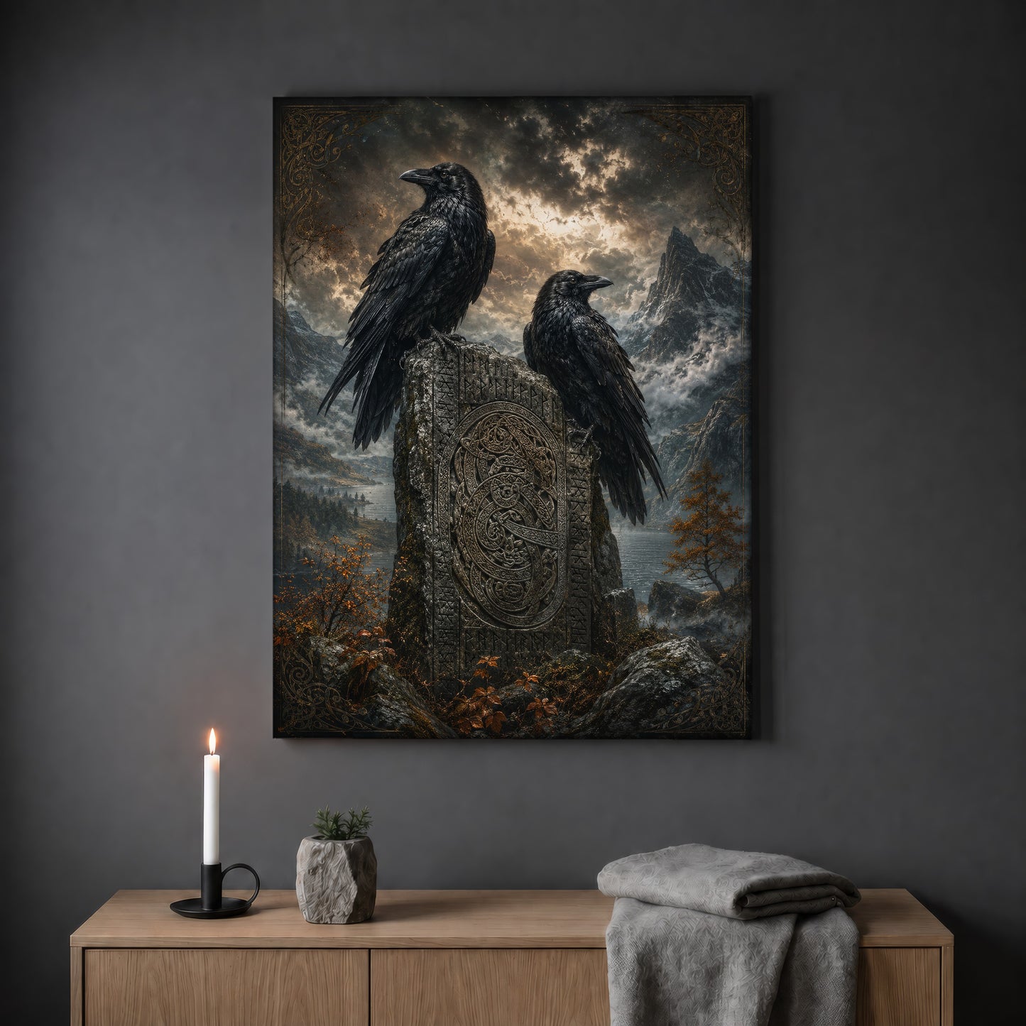 The Watchstone landscape print hanging on a plain grey wall above a light oak sideboard, styled with a lit white taper candle in a black holder, a small stone pot of greenery and a folded grey throw.