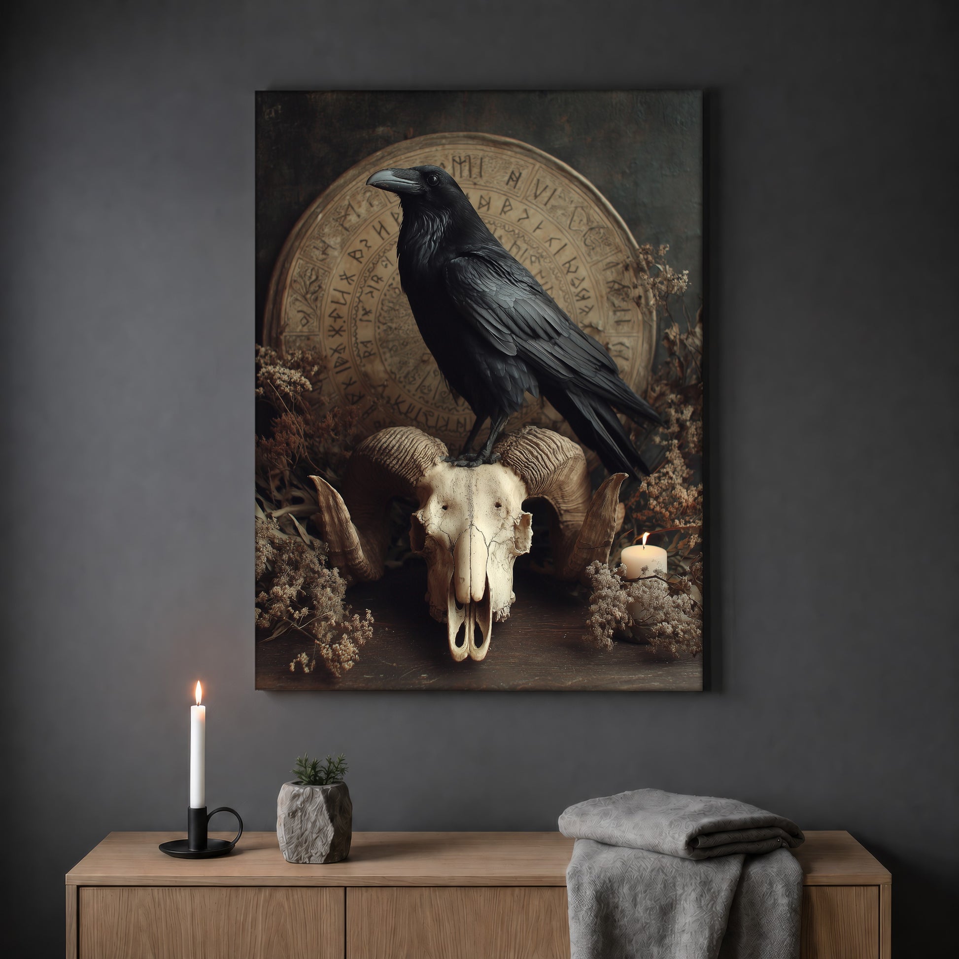 Hrafn still life print hanging on a plain grey wall above a light oak sideboard, styled with a lit white taper candle in a black holder, a small stone pot of greenery and a folded grey throw.