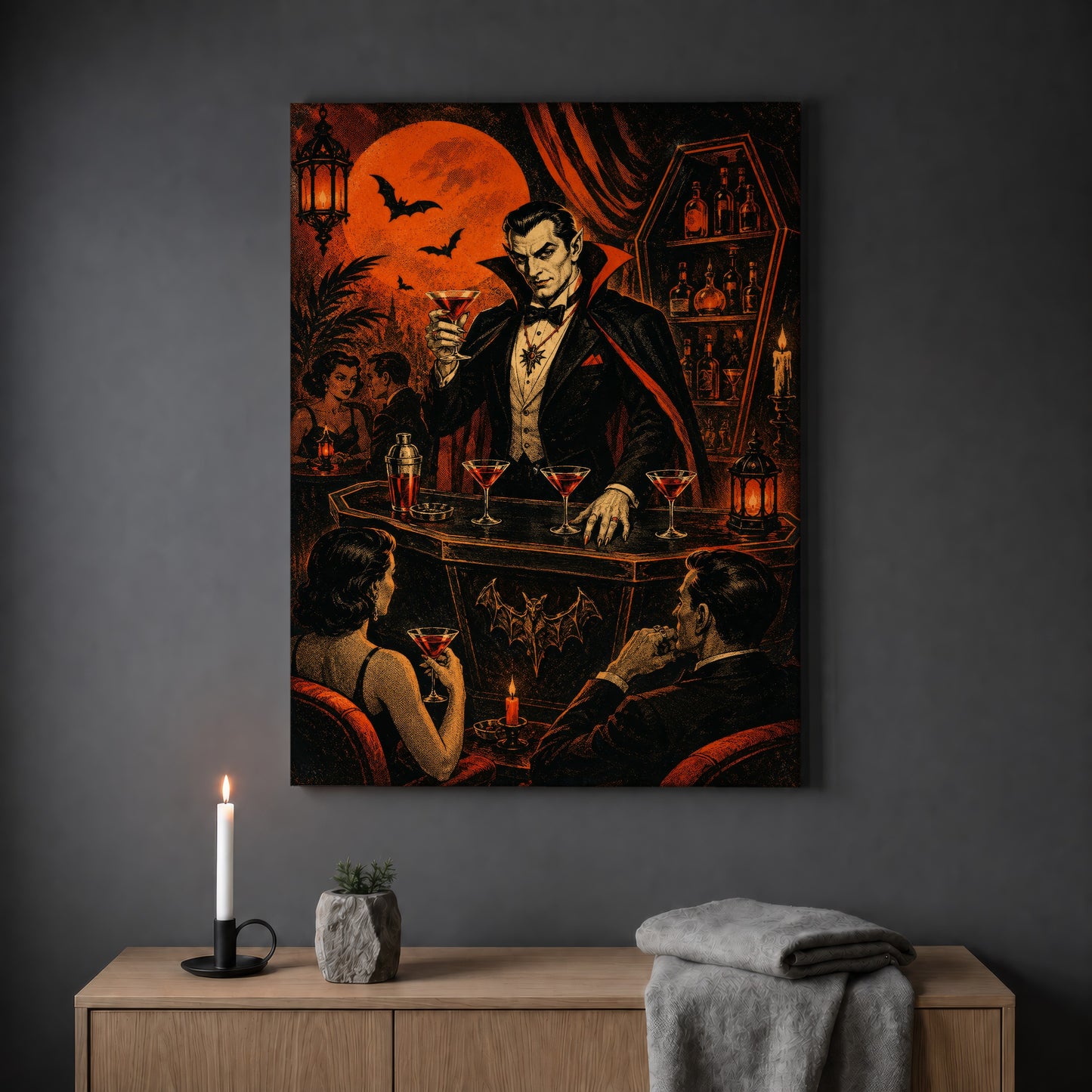Shaken Not Staked cocktail print hanging on a plain grey wall above a light oak sideboard, styled with a lit white taper candle in a black holder, a small stone pot of greenery and a folded grey throw.