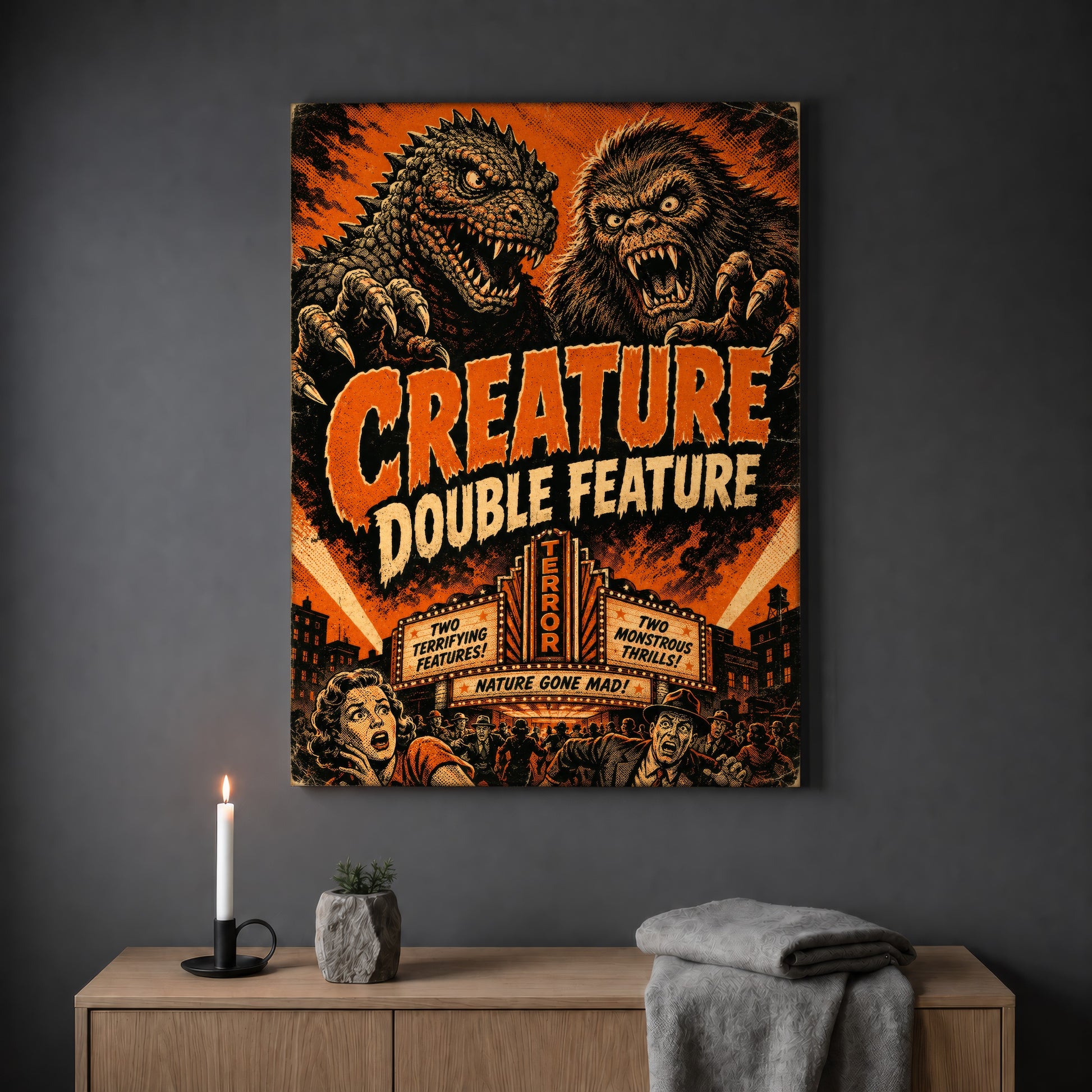 Marquee Mayhem kaiju poster hanging on a plain grey wall above a light oak sideboard, styled with a lit white taper candle in a black holder, a small stone pot of greenery and a folded grey throw.