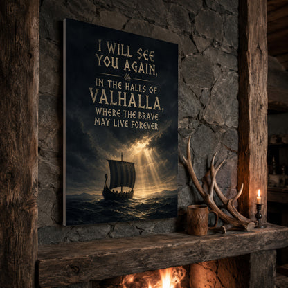 Valhalla Awaits longship print propped at an angle on a rustic stone fireplace mantel framed by timber beams, beside shed antlers, a carved wooden mug and a lit candle, with firelight glowing from the hearth below.