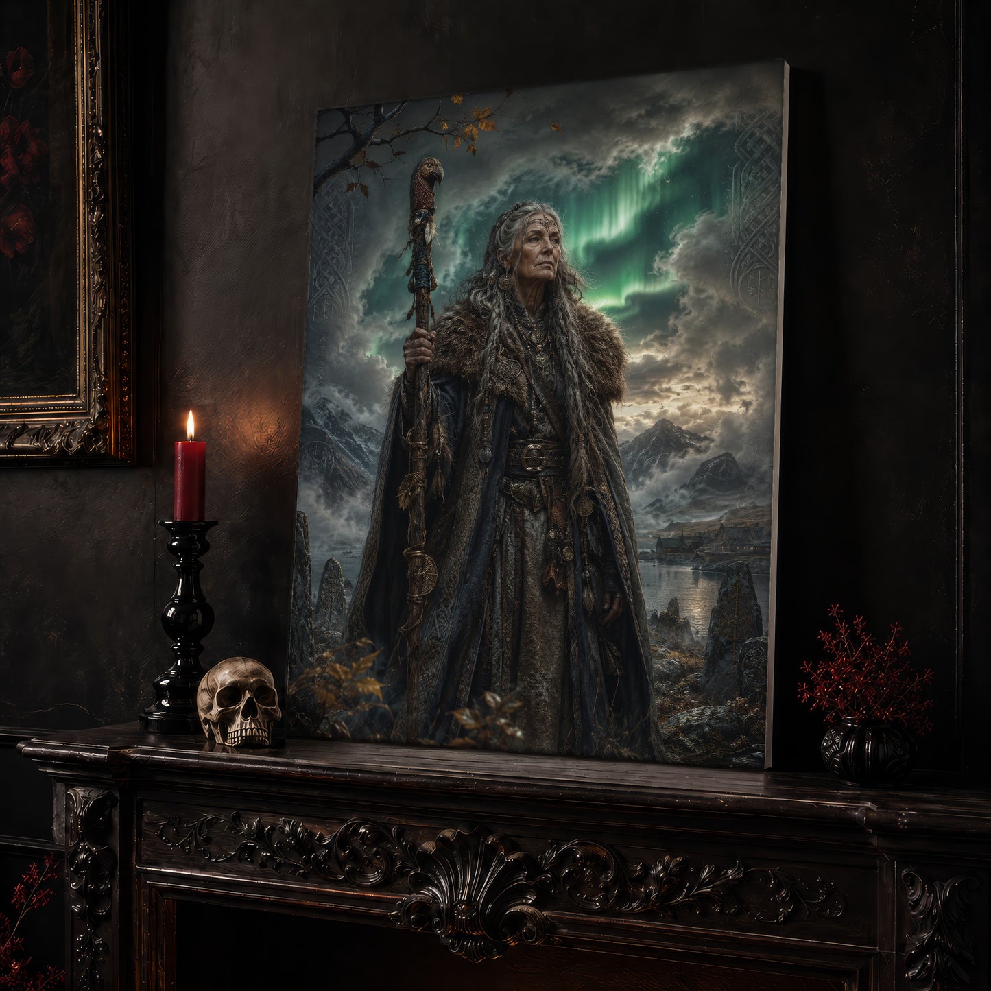 Spákona canvas leaning on a dark carved mantel beside a lit dark red taper in a black candlestick, a bone-coloured skull, and a small black vase of red berry sprigs, with a gilt-framed painting on the wall alongside.