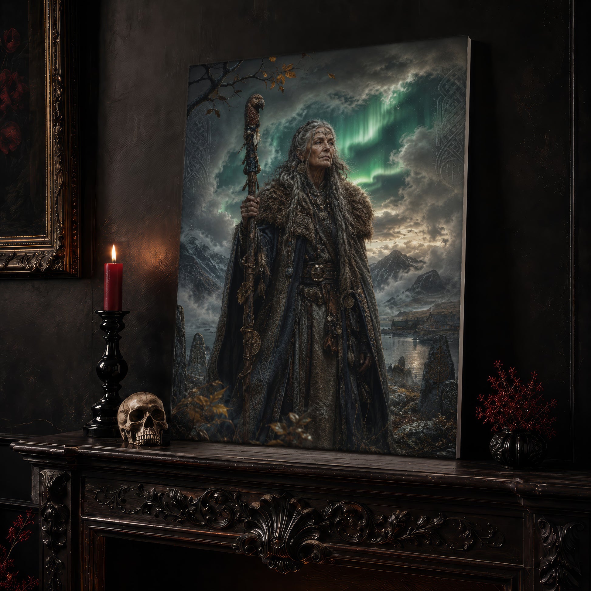 Spákona canvas leaning on a dark carved mantel beside a lit dark red taper in a black candlestick, a bone-coloured skull, and a small black vase of red berry sprigs, with a gilt-framed painting on the wall alongside.