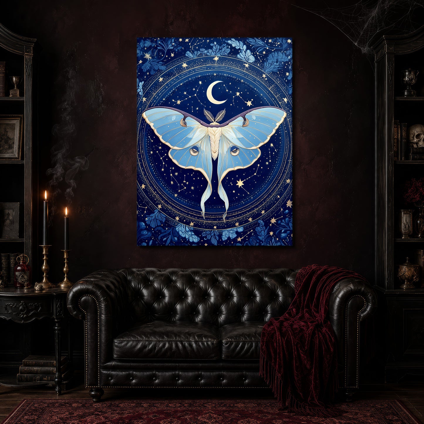 The Blue Hour cobalt moth canvas hanging above a black tufted Chesterfield sofa draped with a red fringed velvet throw, in a cobwebbed oxblood parlour with brass candlesticks, dark cabinets of books and goblets, and a patterned red rug.